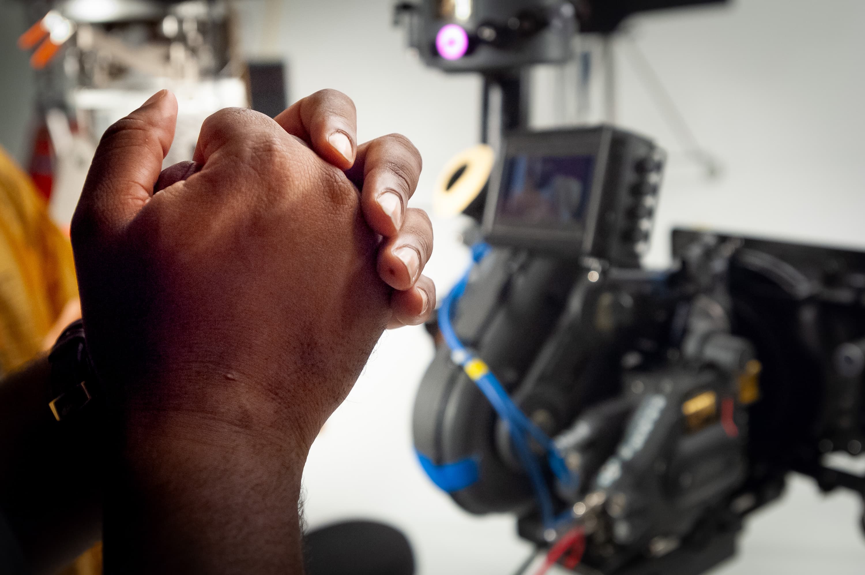 Close up of director Dr. Teeth's hands clasped together with a movie camera out of focus in the background.