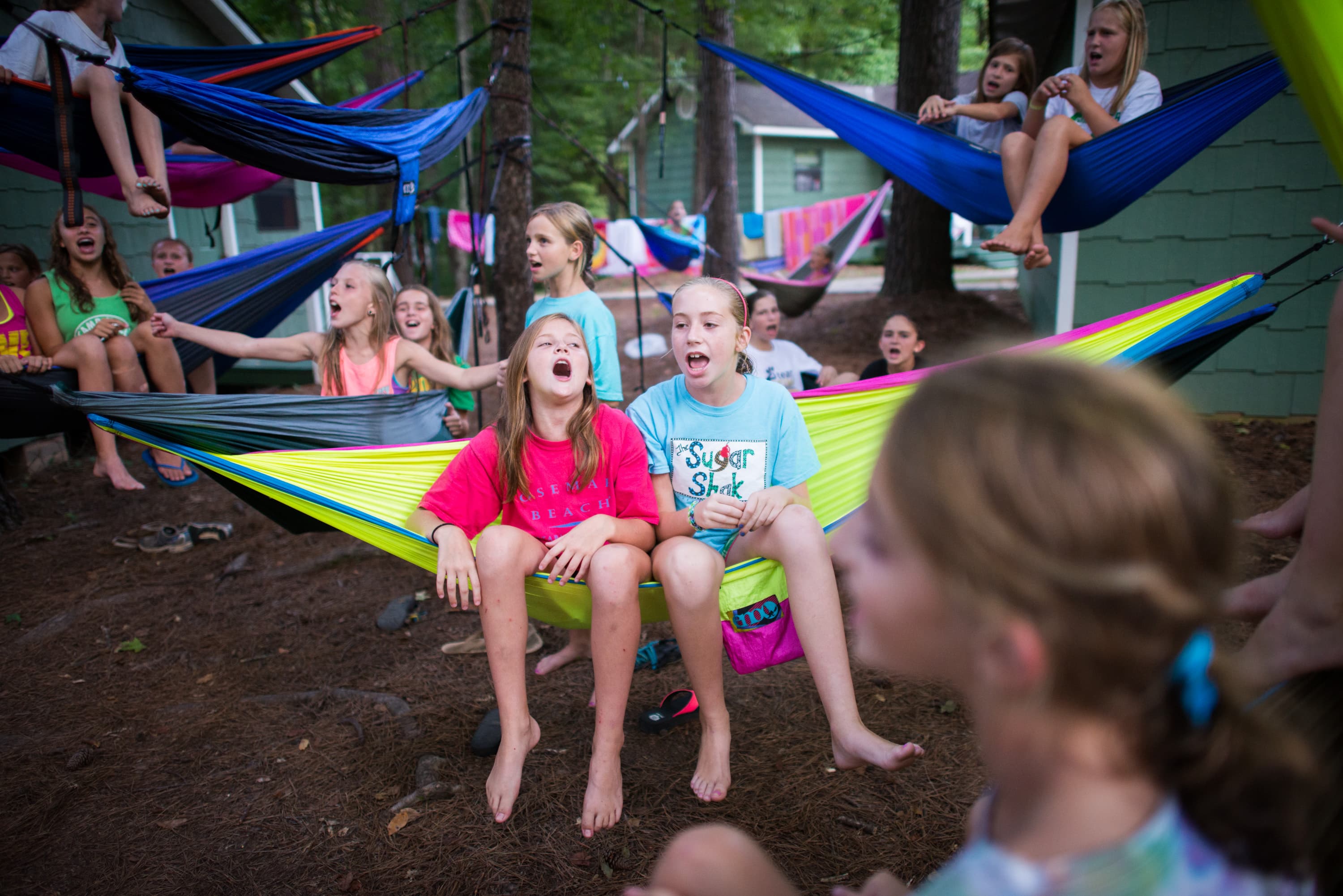 A group of children sitting and playing on colorful hammocks tied between trees in an outdoor setting.