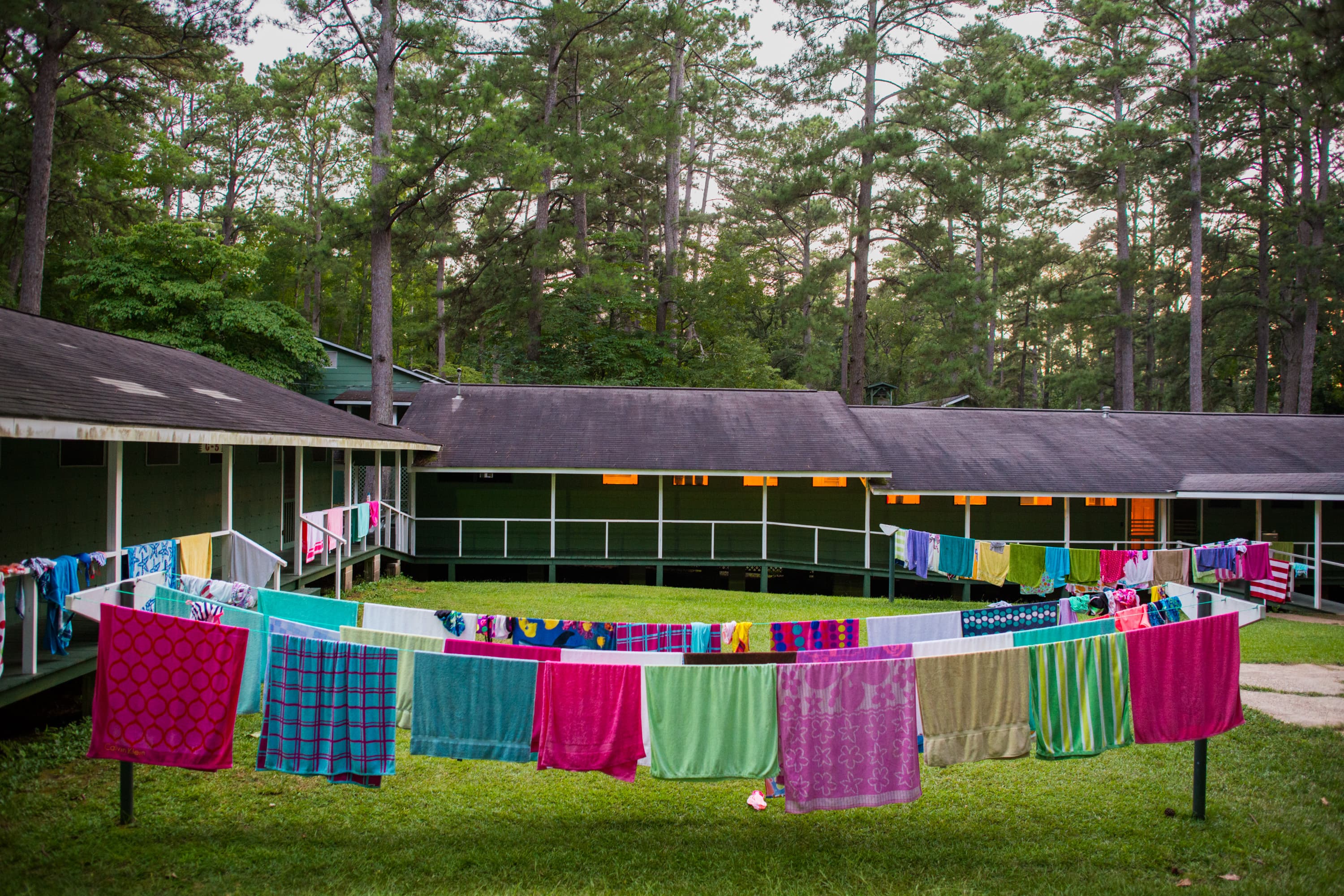 Multiple colorful towels hanging on a clothesline in the courtyard between two green buildings surrounded by trees.